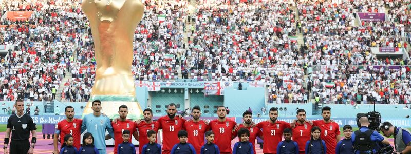 Spieler des Iran stehen beim Abspielen der Nationalhymne vor dem übergroßen Weltpokal im Stadion in Katar. - Foto: Han Yan/XinHua/dpa