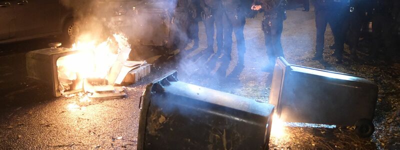 Polizisten stehen bei einer Demo an brennenden Müllcontainern. - Foto: Sebastian Willnow/dpa