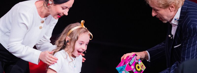 Amelia (M) erhält beim RTL-Jahresrückblick «Menschen, Bilder, Emotionen 2022» ein Geschenk von Moderator Thomas Gottschalk, daneben steht ihre Mutter. - Foto: Rolf Vennenbernd/dpa
