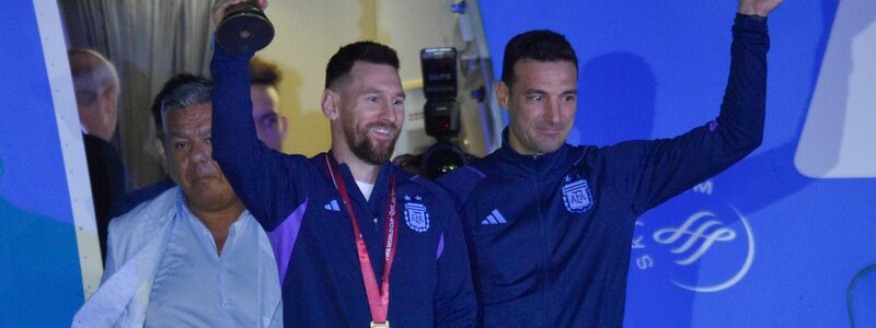 Lionel Messi (l) hält den Weltmeisterpokal in der Hand, während er mit seinem Trainer Lionel Scaloni aus dem Flugzeug aussteigt. - Foto: Gustavo Garello/AP/dpa