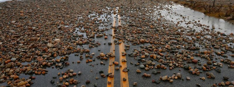 Hohe Wellen haben in Westport (Massachusetts) an der Atlantikküste Steine auf eine Straße gewirbelt. - Foto: Peter Pereira/The Standard-Times/AP/dpa