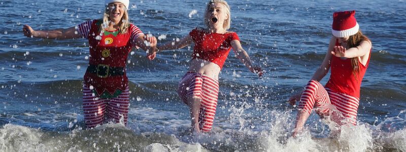Eine Gruppe junger Frauen in Weihnachtskostümen planscht während des jährlichen Weihnachtsschwimmens am Long Sands Beach. - Foto: Owen Humphreys/PA Wire/dpa