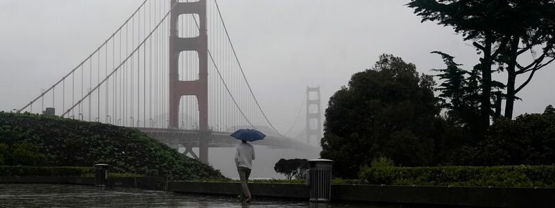 Eine Person versucht in San Francisco, sich  unter einem Schirm vor Regen zu schützen. - Foto: Jeff Chiu/AP/dpa