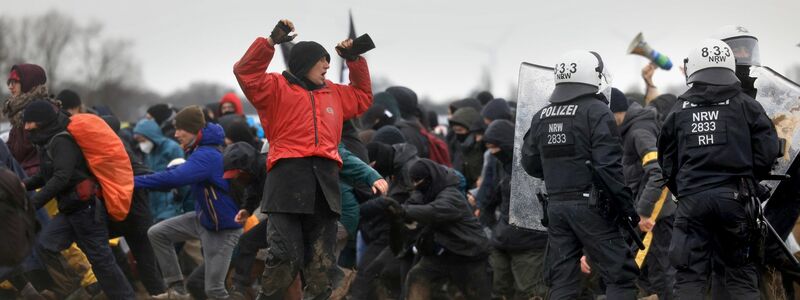 Ein Mann steht mit erhobenen Armen vor Polizisten, hinter ihm rennen weitere Demonstranten. - Foto: Oliver Berg/dpa