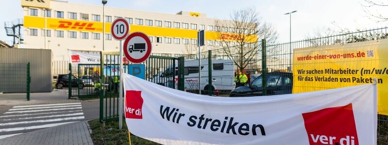 Ein Banner mit der Aufschrift «Wir streiken» hängt vor einem Gebäude des Paketdienstleisters DHL in Lahn. - Foto: Philipp von Ditfurth/dpa