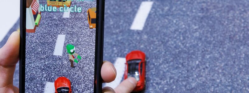 Mittels Smartphone, welches ein reales Spielzeugauto mit der Kamera erfasst, wird beim Spiel «Zombie Crasher AR» von Augmented Robotics eine virtuelle Straßenszene dargestellt. - Foto: Daniel Karmann/dpa
