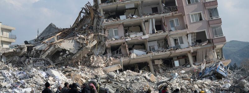 Menschen zwischen den Trümmern eines Wohngebiets in Antakya. - Foto: Boris Roessler/dpa