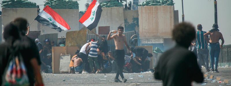 Regierungsgegner vor einer Barrikade der Polizei in Bagdad. - Foto: Hadi Mizban/AP/dpa