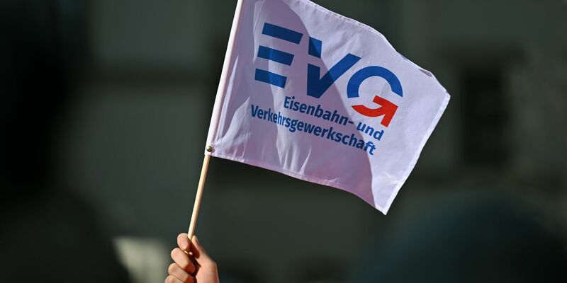 Ein Teilnehmer am Warnstreik Ende März vor dem Erfurter Hauptbahnhof mit einem Fähnchen der Eisenbahn- und Verkehrsgewerkschaft (EVG). - Foto: Martin Schutt/dpa