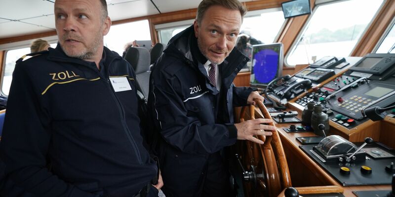 Finanzminister Christian Lindner (r) steuert das Zollboot «Kehrwieder», links Zollkapitän Steffen Molter. - Foto: Marcus Brandt/dpa