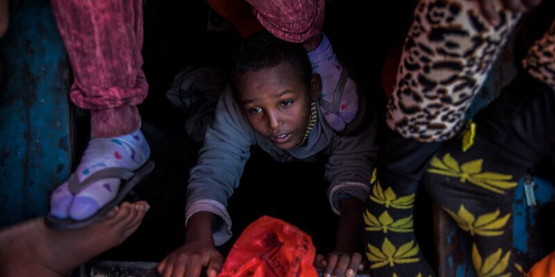 Ein Flüchtlingskind aus Eritrea versucht an der Küste zu Libyen, an Bord eines überfüllten Holzbootes hinaufzuklettern. - Foto: Santi Palacios/AP/dpa