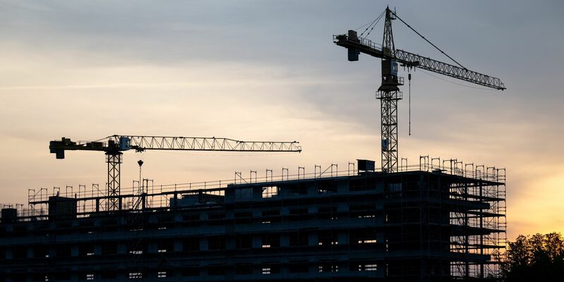 Kräne stehen hinter dem Rohbau für ein Bürogebäude auf einer Baustelle. Die Flaute am Bau hat sich auch im März fortgesetzt. - Foto: Hendrik Schmidt/dpa