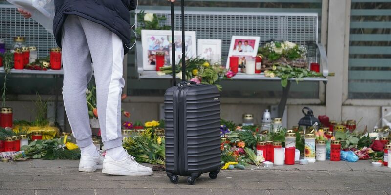 Eine Reisende schaut sich die Blumen, Kerzen und verschiedene Bilder im Wartehäuschen am Bahnhof zum Gedenken an die Opfer der Messerattacke an. - Foto: Marcus Brandt/dpa