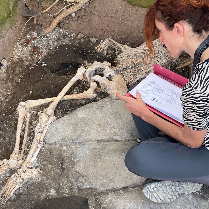 Eine Frau sitzt vor einem Skelett im Archäologiepark Pompeji. - Foto: -/Archäologiepark Pompeji/dpa