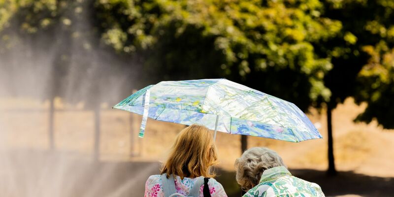 Zwei Frauen schützen mit einem Regenschirm vor der Sonne. - Foto: Rolf Vennenbernd/dpa