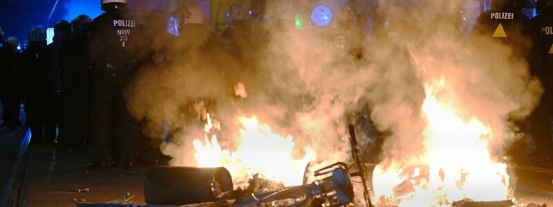 Polizisten hinter einer brennenden Barrikade. - Foto: Robert Michael/dpa