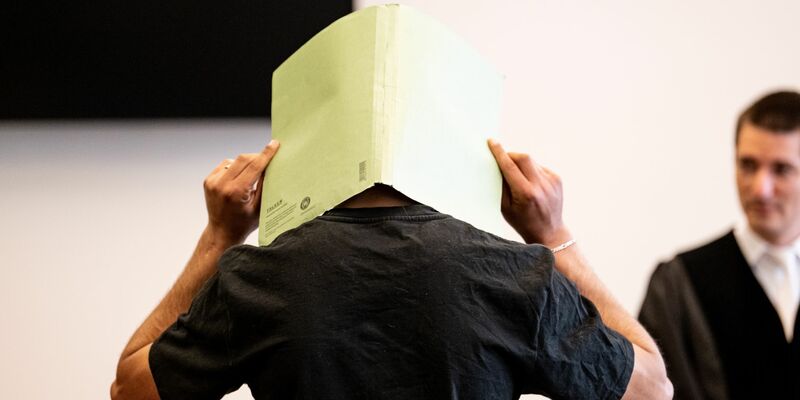 Der Angeklagte (M) verbirgt im Gerichtssaal sein Gesicht hinter einer Aktenmappe. - Foto: Fabian Sommer/dpa