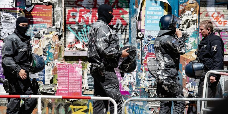 Mit Farbe beworfene Polizeibeamte verlassen das Haus Nr. 94 in der Rigaer Straße in Berlin. - Foto: Paul Zinken/dpa-Zentralbild/dpa