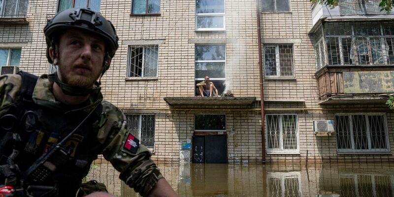 Ein Mann kocht auf einem offenen Feuer auf einer Veranda vor dem Eingang eines mehrstöckigen Gebäudes in einem überfluteten Viertel. - Foto: Evgeniy Maloletka/AP/dpa