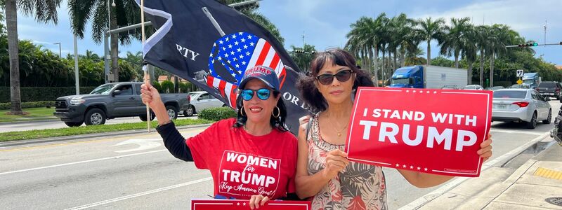 Zwei Trump-Anhängerinnen empfangen den Ex-Präsidenten vor seinem Hotel in Miami mit Schildern, auf denen «Ich stehe hinter Trump» geschrieben steht. - Foto: Magdalena Tröndle/dpa