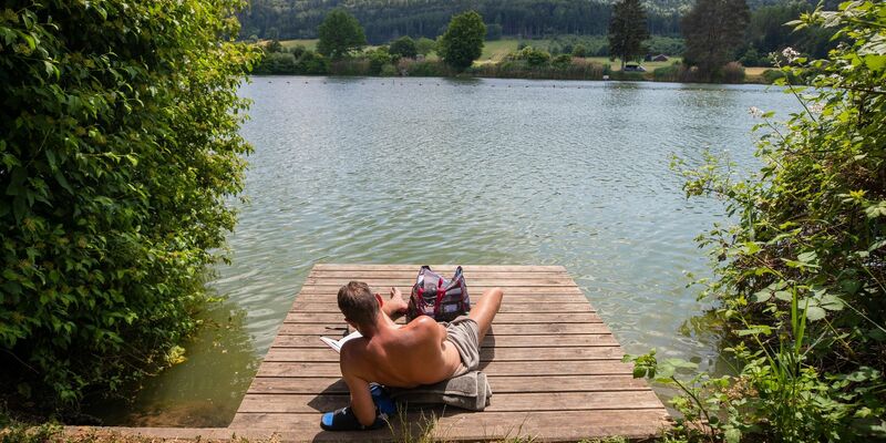Ein Mann genießt die Sonne am Badesee Plüderhausen - und vielleicht auch den ein oder anderen Sommerhit. - Foto: Christoph Schmidt/dpa