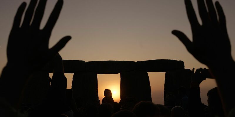 Menschen versammeln sich bei Sonnenaufgang am Tag der Sommersonnenwende um den Heel Stone in Stonehenge. - Foto: Kin Cheung/AP