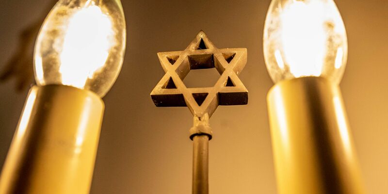 Ein siebenarmiger Leuchter (Menora) mit einem Davidstern in der Mitte leuchtet in einer Synagoge. Fragen zum Judentum werden auf einer Website beantwortet. - Foto: David Inderlied/dpa
