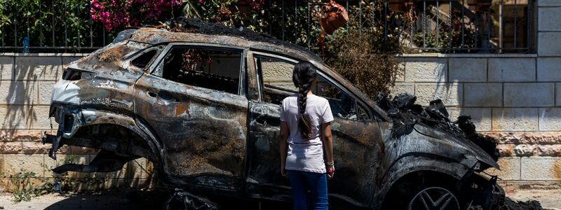 Ein Mädchen steht in Turmus Aya im Westjordanland neben einem Auto, das infolge eines Brandanschlags durch jüdische Siedler zerstört worden ist. - Foto: Ilia Yefimovich/dpa