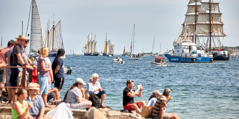 Menschen verfolgen an der Förde die Windjammerparade. - Foto: Georg Wendt/dpa