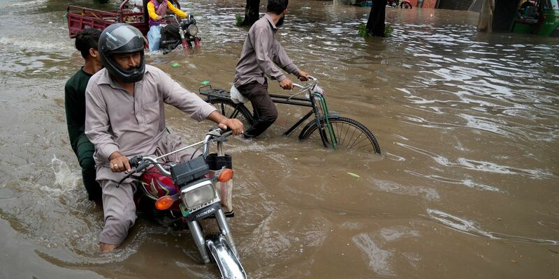 Motorradfahrer auf einer überschwemmten Straße im pakistanischen Lahore. - Foto: K.M. Chaudary/AP/dpa