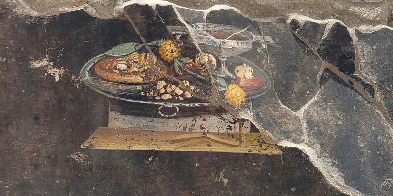 Die Wand eines pompejanischen Hauses mit einem Fresko, das einen Tisch mit Speisen darstellt, darunter auch eine Art Pizza. - Foto: ---/Pompeii Archaelogical Park/AP/dpa