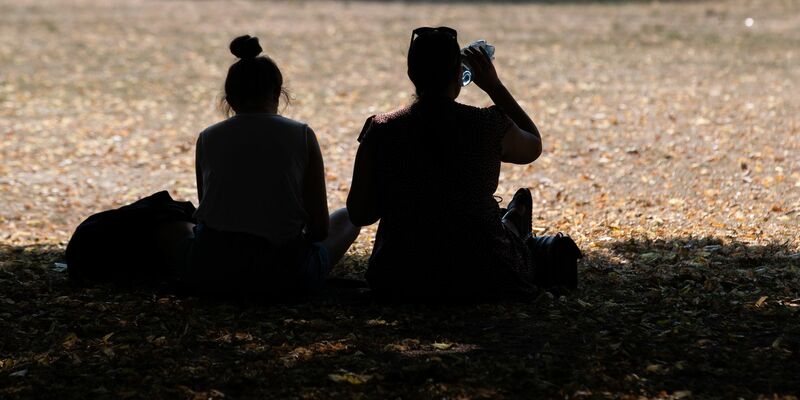 Zwei Frauen sitzen in einem Park im Schatten der Bäume, um sich vor der Hitze zu schützen. - Foto: Friso Gentsch/dpa