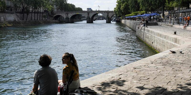 Zwei junge Leute sitzen am Ufer der Seine in Paris. - Foto: Alain Jocard/AFP/dpa