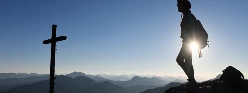 Eine Ausflüglerin genießt den Blick am Gipfelkreuz des Taubensteins. - Foto: Tobias Hase/dpa