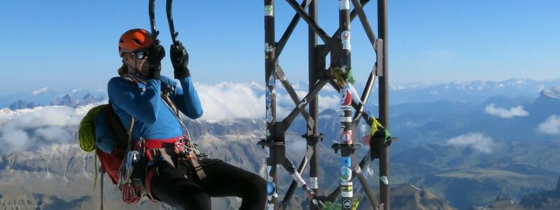 Ein Bergsteiger macht an seinen Eisgeräten einen Klimmzug am Gipfelkreuz der Marmolada. - Foto: Elke Richter/dpa