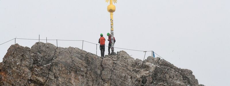 Bergsteiger stehen neben dem Gipfelkreuz des Zugspitzgipfel. - Foto: Felix Hörhager/dpa