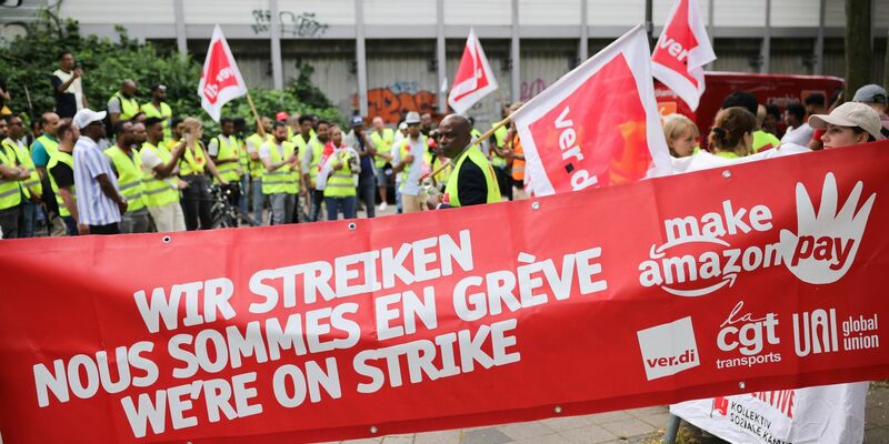Beschäftigte von Amazon bei einer Demonstration unter dem Titel «Make Amazon Pay! Für gute und gesunde Arbeit bei Amazon!» vor dem Amazon-Verteilzentrum in Hamburg-Veddel. - Foto: Christian Charisius/dpa