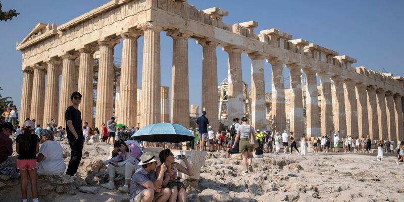 Touristen unter einem Sonnenschirm vor der Akropolis, die inzwischen geschlossen wurde. - Foto: Petros Giannakouris/AP/dpa