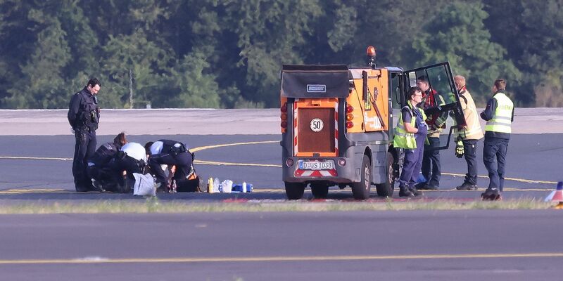 Sicherheitspersonal und Polizisten versuchen am Düsseldofer Flughafen, Aktivisten vom Asphalt auf dem Rollfeld zu lösen. - Foto: David Young/dpa