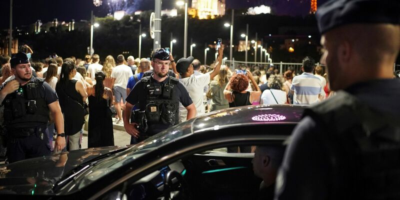 Polizisten kontrollieren einen Autofahrer in Lyon, während die Menschen ein Feuerwerk zum Tag der Bastille beobachten. - Foto: Laurent Cipriani/AP
