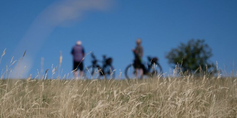 Zwei Radfahrer stehen am Rand der Schwäbischen Alb vor einer trockenen Wiese. - Foto: Marijan Murat/dpa