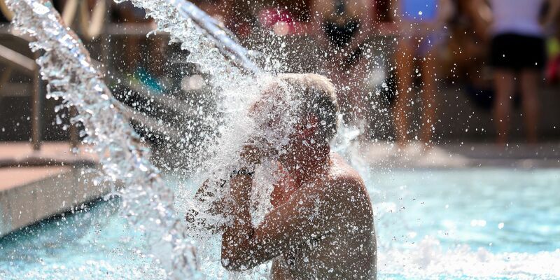 Ein Mann erfrischt sich im Donaubad in Sigmaringen unter einer Wasserfontäne. - Foto: Thomas Warnack/dpa