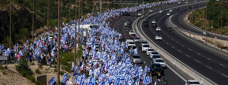 Tausende israelische Demonstranten marschieren entlang einer Autobahn, um gegen die geplante Justizreform der Regierung zu protestieren. - Foto: Ohad Zwigenberg/AP/dpa