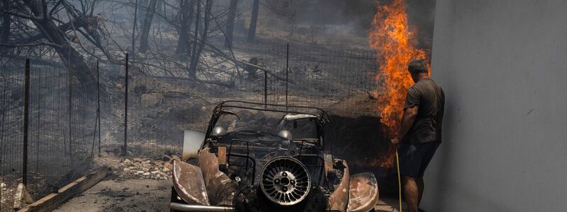 Ein Bewohner versucht, die Flammen im Hof eines Hauses auf der Ägäisinsel zu löschen. - Foto: Petros Giannakouris/AP/dpa