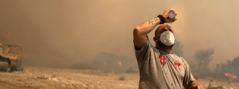 Ein Helfer kühlt sich während eines Waldbrandes in der Ortschaft Vati ab. - Foto: Petros Giannakouris/AP/dpa