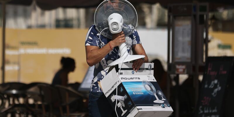 Ein Mann trägt einen Ventilator, während er bei 38 Grad Celsius über die Place de la Comedie in Montpellier geht. - Foto: Gao Jing/XinHua/dpa
