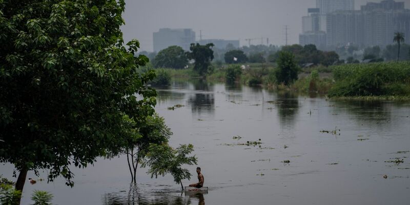 Ein Junge sitzt auf einem Schild in der Nähe einer Wohnkolonie, die vom Hochwasser des Flusses Hindon überschwemmt wurde. - Foto: Altaf Qadri/AP/dpa