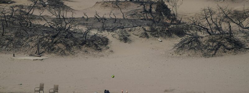 Hinten die verbrannte Vegetation, vor das Mittelmeer. Eine Frau spielt mit einem Ball am Strand bei Gennadi auf Rhodos. - Foto: Petros Giannakouris/AP