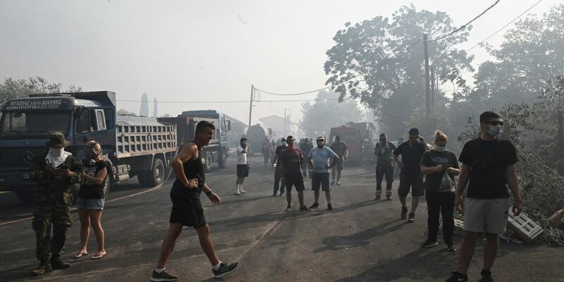 Verunsicherte Anwohner auf einer Straße in Nea Anchialos. Wegen der starken Rauchbildung flüchteten viele Urlauber an den örtlichen Strand. - Foto: Tatiana Bolari/Eurokinissi/AP/dpa