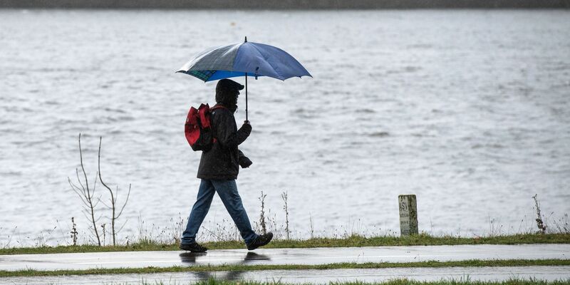 Spaziergänger mit Regenschirm am Ufer des Kemnader Sees in Bochum. - Foto: Bernd Thissen/dpa